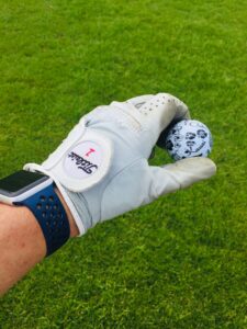 Close-up of a golf glove holding a uniquely designed golf ball on a vibrant green lawn.